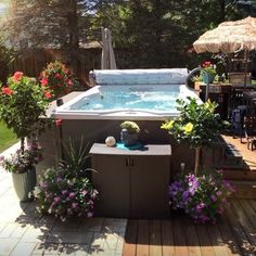 an outdoor hot tub surrounded by potted plants and flowers on a deck with umbrellas