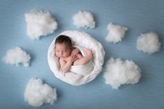 a baby wrapped in a blanket is surrounded by clouds and rainbows on a blue background