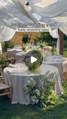 a table set up with white linens and greenery for a wedding reception in the grass