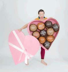 a woman holding a pink heart shaped box filled with chocolates and macaroons