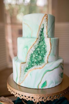 a three tiered cake with green and white marble on it's side, sitting on a gold stand