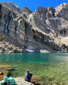 a person sitting on top of a rock next to a lake with mountains in the background