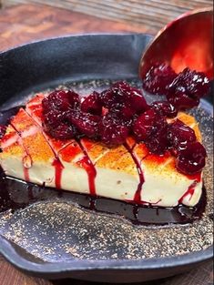 a piece of cheesecake with berries on top is being drizzled with sauce