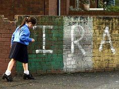 a woman walking past a brick wall with graffiti on it