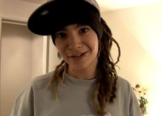 a girl with dreadlocks and a baseball cap smiles while wearing a t - shirt