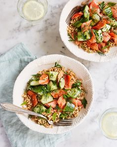 two white bowls filled with rice, cucumber and salmon on top of a marble table