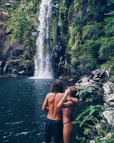 two people are standing in front of a waterfall and looking at the water from below