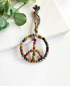 a peace sign made out of colorful beads on a white surface next to a green plant