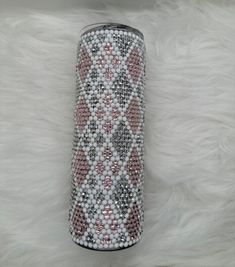 a pink and white can with some silver beads on the side sitting on a furry surface