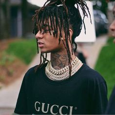 a young man with dreadlocks standing in front of another person wearing a gucci t - shirt