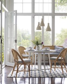 a white table with four chairs and a vase on it in front of large windows