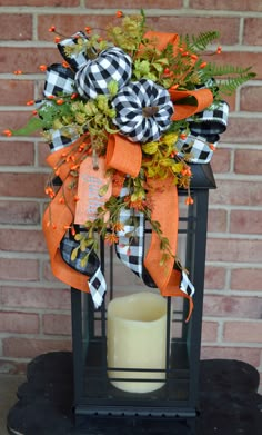 an orange and black fall wreath on top of a lantern with a candle in it