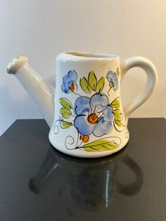 a ceramic teapot with blue flowers painted on the front and sides, sitting on a black table