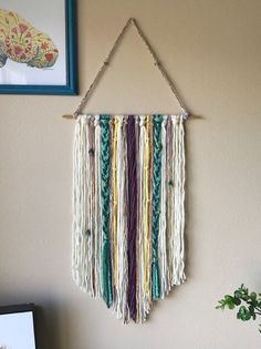 a wall hanging made out of macrame and yarn with a plant next to it