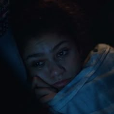 a woman laying down in the dark with her hand on her face and looking at something