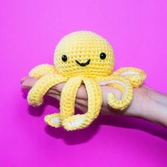 a crocheted yellow octopus stuffed animal in someone's hand on a pink background