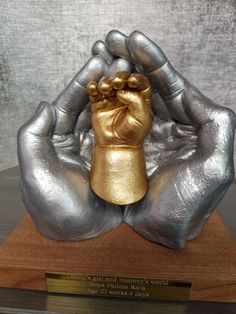 a gold and silver hand statue on top of a wooden base with a plaque in front of it