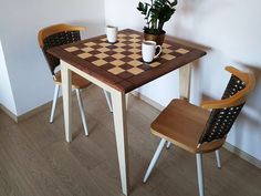 a small table with two chairs and a checkerboard pattern on the top is next to a potted plant