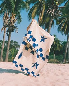 a blue and white checkered beach towel on the sand with palm trees in the background