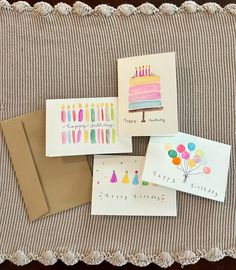 four birthday cards on a table with envelopes and one has a slice of cake