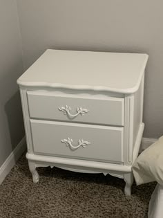 a white dresser sitting next to a bed on top of a carpeted bedroom floor