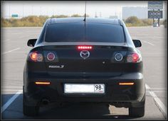 the back end of a black car in a parking lot with its lights turned on