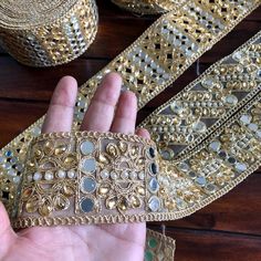 a hand is holding some gold and silver beaded trims on a wooden surface