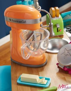 an orange mixer sitting on top of a wooden table next to other kitchen accessories and utensils