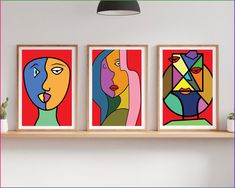 three framed paintings on a wall above a shelf