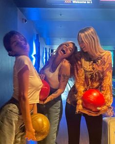 three women standing in front of a bowling alley holding red and yellow balls with their mouths open