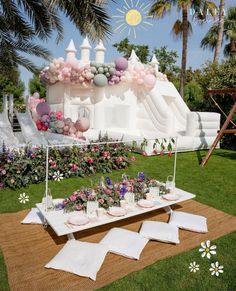 a table set up for a party with balloons and flowers on the grass near an inflatable castle