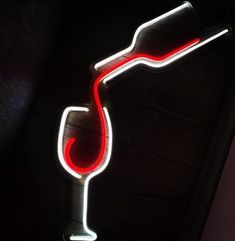 a red wine glass neon sign hanging from the side of a dark room with black walls