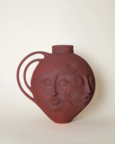 a red vase sitting on top of a white table next to a black object in the shape of a woman's face