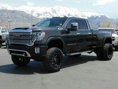 a large black truck parked in a parking lot next to other trucks and snow covered mountains