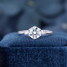 a three stone diamond ring on top of a blue velvet cushion