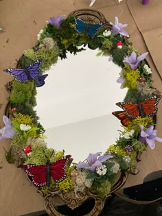 a mirror that is sitting on top of a table with flowers and butterflies around it