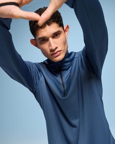 a young man is holding his hands behind his head and posing for the camera while wearing a blue shirt