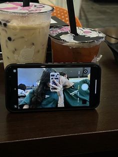 a cell phone sitting on top of a wooden table next to two cups of coffee