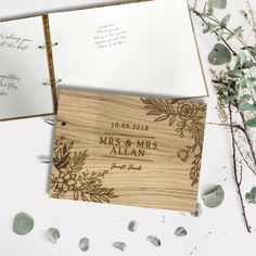 an open wooden wedding album with flowers and leaves on the cover, surrounded by greenery