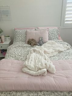 an unmade bed with pink comforter and pillows on it, next to a window