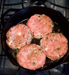 four hamburger patties cooking in a skillet on top of the gas stovetop