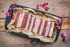 a cake with red and white frosting in a pan on a wooden table next to raspberries