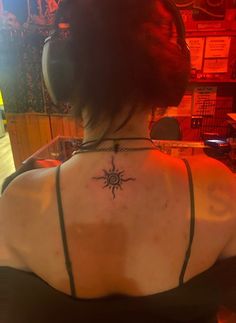 the back of a woman's neck with a sun tattoo on her left shoulder