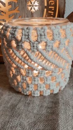 a crocheted candle holder sitting on top of a table next to a wooden barrel