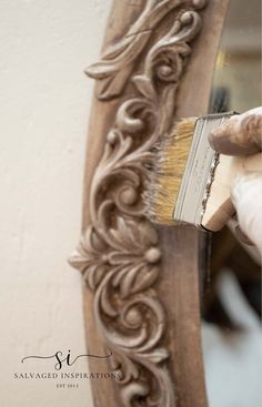 a person is holding a paintbrush in front of a carved frame with an ornate pattern on it