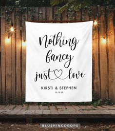 a wedding banner hanging on the side of a wooden fence with string lights around it