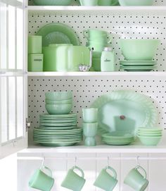 green dishes and cups are on shelves in a white room with polka dot wallpaper