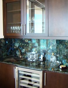 a kitchen with wooden cabinets and green marble counter tops, wine glasses on the cabinet doors