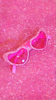 a pair of pink sunglasses laying on top of a pink floor covered in flecky glitter