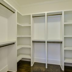 an empty walk in closet with white walls and open shelves on the wall, along with hardwood flooring